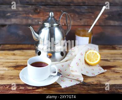 Tasse schwarzer Tee mit Zitrone, Teekanne und Marmelade auf dem hölzernen Hintergrund Stockfoto