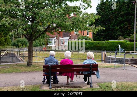 Rückansicht von drei älteren Menschen, alle mit weißem Haar zwei Frauen, ein Mann, der auf einer Bank am Fluss sitzt, in Shepperton Lock Surrey England, Großbritannien Stockfoto