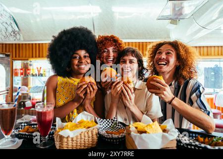 Multiethnische Gruppe von Freunden beim Essen im Vintage Diner Restaurant aus den 80er Jahren - multiethnische junge Leute, die sich zusammenschließen und Spaß haben, in einem amerikanischen Fastfood essen Stockfoto