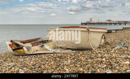 Ein kaputtes Boot am Kiesstrand von Herne Bay, Kent, England, Großbritannien, mit Herne Pier im Hintergrund Stockfoto