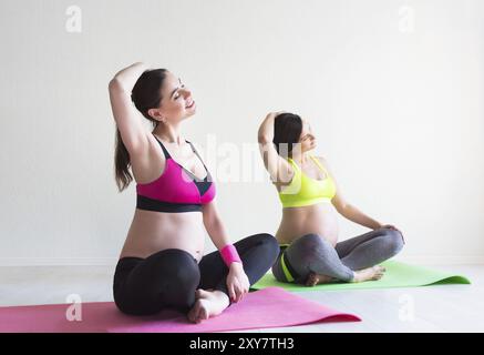 Zwei junge schwangere Frauen machen Yoga-Übungen im Studio Stockfoto