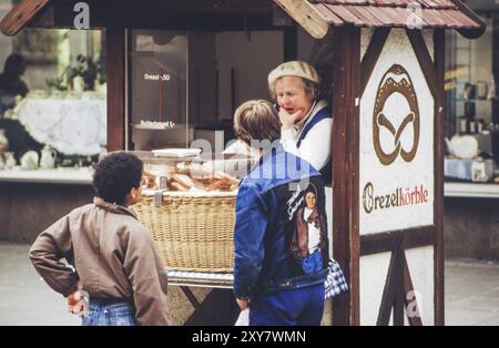 Ältere Verkäuferin in einem Verkaufsstand, der Brezelkörbe in der Königstraße verkauft, vor ihren beiden Kindern, eines trug eine Michael Jackson Denim Jacke, das OT Stockfoto