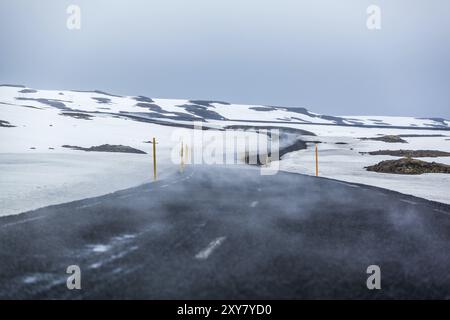 Eine Nebelspur zieht sich über eine gekrümmte Asphaltstraße durch eine verschneite Landschaft Stockfoto