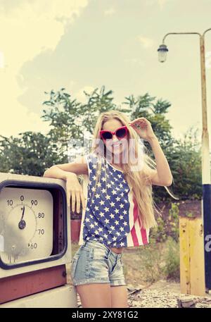 Blondes Mädchen hält Hände auf ihre Brille auf beschädigte Tankstelle stehend Stockfoto