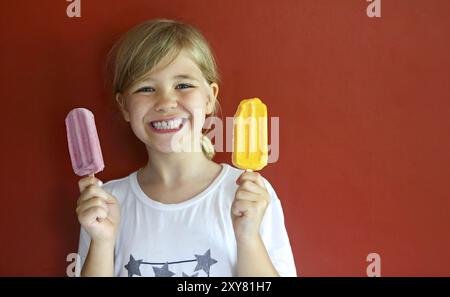 Kleine blonde Mädchen Eis essen auf dem roten Hintergrund Stockfoto