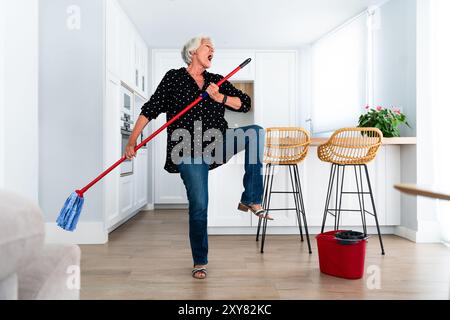 Schöne ältere Frau mit grauen Haaren zu Hause, die Spaß beim Putzen hat - Jugendliche ältere Oma verbringt gute Zeit zu Hause Stockfoto