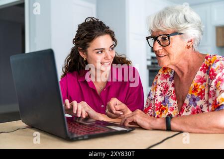 Schöne Großmutter und Enkelin zu Hause und lernen, wie man Computer benutzt - fröhliche Oma und Neffe verbringen gute Zeit zusammen Stockfoto