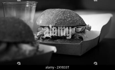 Köstlicher Käse, Käse-Beef-Burger mit Salat, Tomate und Käse darin. Street Food. Fleischschnitzel-Burger sind in Papierkartons. Lieferung von Lebensmitteln Stockfoto