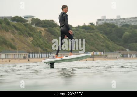 Ein junger Mann in einem Neoprenanzug reitet im Meer und fliegt über dem Wasser auf einem elektrisch betriebenen Tragflächenbrett, einer Hybridfolie mit Eoil-Folienantrieb Stockfoto