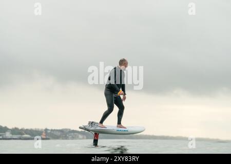 Ein Mann mittleren Alters in einem Neoprenanzug reitet im Meer und fliegt über dem Wasser auf einem elektrisch betriebenen Tragflächenbrett, einer Hybridfolie mit Eoil-Folienantrieb Stockfoto