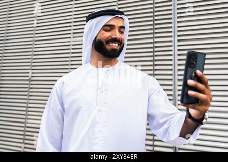 Porträt eines gutaussehenden arabischen Geschäftsmannes mit traditionellem emirat-Kandura - männlicher Erwachsener aus dem Nahen Osten mit Dschdasha mit Smartphone-Gerät Stockfoto