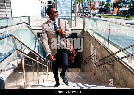 Reifer schwarzer Geschäftsmann in elegantem Anzug, der durch die Stadt schlendert - ein Erwachsener in afrika mit grauem Bart, der mit U-Bahn-Trans reist Stockfoto