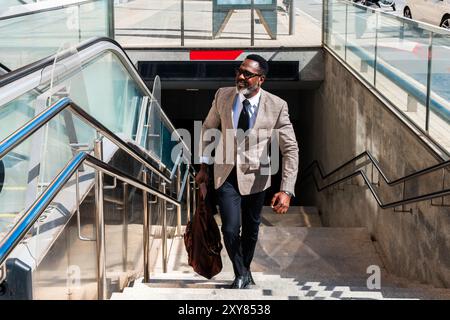 Reifer schwarzer Geschäftsmann in elegantem Anzug, der durch die Stadt schlendert - ein Erwachsener in afrika mit grauem Bart, der mit U-Bahn-Trans reist Stockfoto