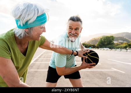 Wunderschönes glückliches Seniorenpaar, das Basketball spielt und Spaß hat - reifes verheiratetes Paar, das verliebt ist, sich im Freien zu verbinden und gemeinsam Sport zu treiben, Konzepte ab Stockfoto
