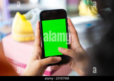 Schöne junge hispanische Frau, die ihr E-Commerce-Geschäft für Hausbekleidung von zu Hause aus verwaltet - Online-Shop, Nahaufnahme auf dem Handy-Green Screen Stockfoto