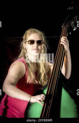 Musiker mit rotem Hemd spielt einen Kontrabass vor schwarzem Hintergrund Stockfoto