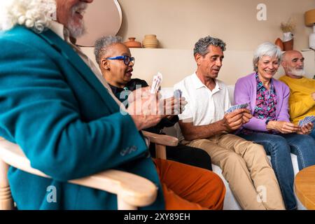 Eine Gruppe glücklicher Seniorenfreunde, die sich zu Hause für eine Dinnerparty zusammenschließen - fröhliche und Jugendliche alte, reife, multiethnische Leute, die Spaß haben Stockfoto