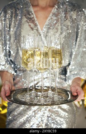 Nahaufnahme der jungen Frau tragen Cocktail Kleid mit Fach der glänzende Gläser Champagner über Schwarz, Weiß, goldenen und silbernen Ballons backgroun Stockfoto