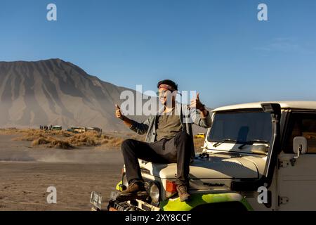 Mann, der den Vulkan Bromo mit dem Jeep besucht und auf der Motorhaube sitzt, Java, Indonesien Stockfoto