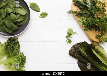 Flach legen mit Schneidebrett und Schüssel mit frischen grünen Salatblättern Spinat und Salat, Romaine und Petersilie, Basilikum auf weißem Hintergrund. Gesundes Gemüse Stockfoto