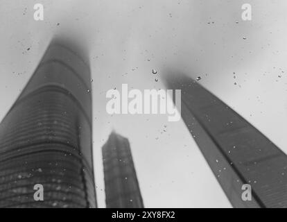 Der flache Blick auf den Shanghai Tower und die benachbarten Wolkenkratzer verschwimmen an einem regnerischen Tag in Wolken, wenn man durch ein Autofenster mit Regentropfen sieht Stockfoto