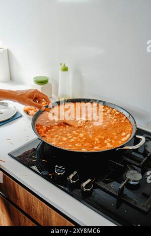 Ein Mann rührt die Paella-Pfanne, wo er eine spanische Fideua kocht, im Herd einer Hausküche Stockfoto