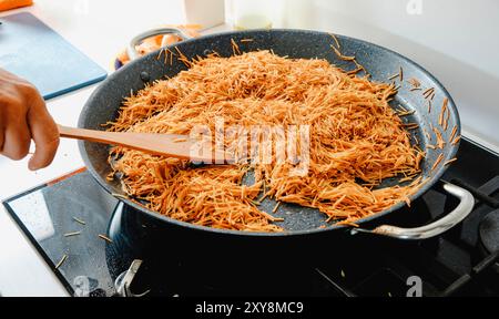 Nahaufnahme eines Mannes, der Nudeln frittiert, um eine spanische Fideua in einer Paella-Pfanne auf dem Herd einer Hausküche zuzubereiten Stockfoto