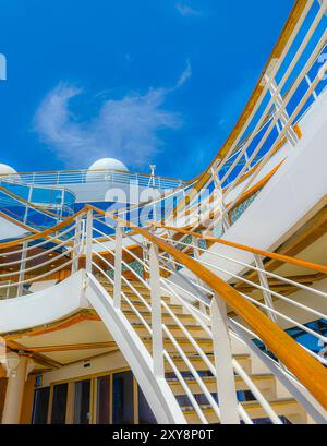 Sehen Sie die Treppe draußen auf einem Kreuzfahrtschiff. Sehen Sie den blauen Himmel mit Wolken darüber. Siehe saubere, weiße Geländer auf den Decks. Versandfertig. Stockfoto