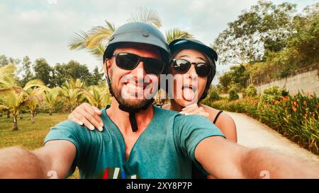 Porträt das verrückte authentische junge glückliche kaukasische Paar macht Smartphone-Selfie, während es Spaß macht, mit dem Roller auf einem tropischen Roadtrip in südostasien zu fahren. Stockfoto