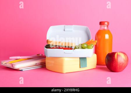 Lunchboxen mit Snacks, Flasche Saft, Wecker und Schreibwaren auf rosa Hintergrund Stockfoto