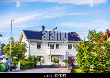 Wunderschöner Blick auf weiße zweistöckige Holzvilla mit Solarpaneelen und schwedischer Flagge auf dem Dach, in einem grünen Wohndorf gelegen. Schweden. Stockfoto