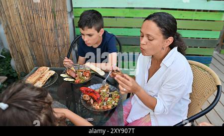 Eine Familie versammelt sich an einem Tisch im Freien für ein gemütliches Essen. Sie führen Gespräche, während sie Essen und ein Gefühl der Zusammengehörigkeit teilen. Stockfoto