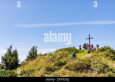 Lenggries, Deutschland. August 2024. Wanderer stehen um ein Gipfelkreuz in den Bayerischen Voralpen. Das Gebiet ist ein beliebtes Ski- und Wandergebiet für Urlauber und Menschen aus der Region München. Vermerk: Frank Hammerschmidt/dpa/Alamy Live News Stockfoto