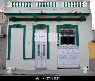 651 elfenbeinfarbene Wand, grüne Zierleisten, Holztür, Gitterfenster, Garagentor aus Metall, Kolonialhaus in der Gemeinde Maceo Street-Regla 406. Havanna-Kuba. Stockfoto