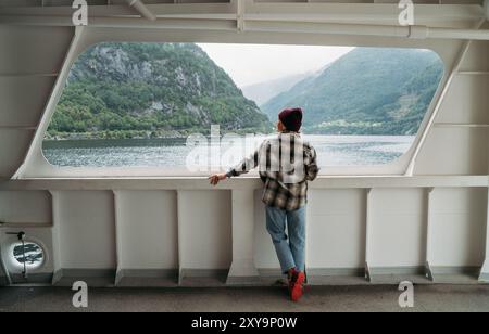 Frau genießt Fjordlandschaften auf der norwegischen Fähre mit nebelgrünen Bergen im Hintergrund. Die Szene fängt das Wesen entspannter Reisen und Erkundungen ein Stockfoto