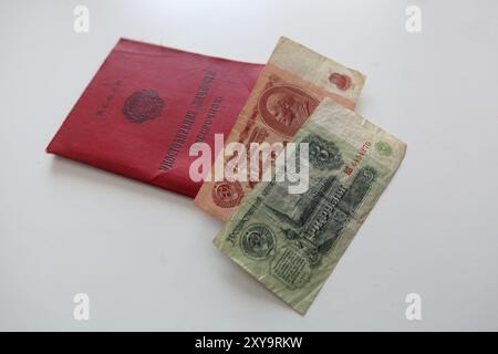 Ein rotes Heft mit der Aufschrift Russische Föderative Sozialistische Republik, Identitätsnachweis und sowjetische Rechnungen, die auf einer weißen Oberfläche ruhen. Stockfoto