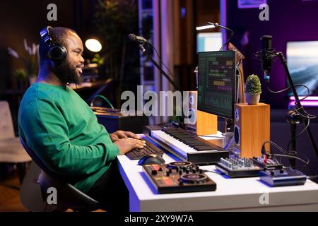 afroamerikanischer Produzent mischt Klänge und Melodien auf seinen Audiodateien und hört sich das Endprodukt über das Headset an. Audiotechniker arbeitet am pc mit DAW-Softwareschnittstelle und Stereoanlage. Stockfoto