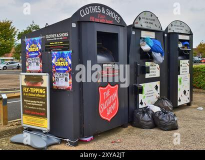 Drei Recyclingbehälter für Kleidung und Schuhe, mit einem Hinweis über das Abkippen von Fliegenfliegen. Stockfoto