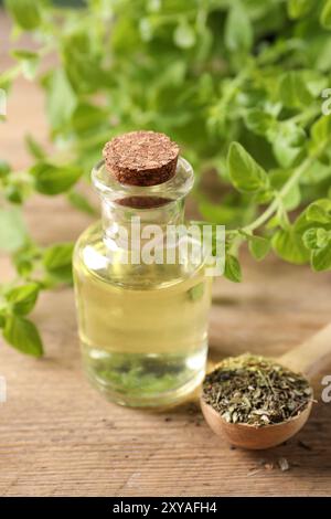 Ätherisches Öl in der Flasche, Löffel mit trockenem Kraut und Oregano-Zweigen auf Holztisch, Nahaufnahme Stockfoto