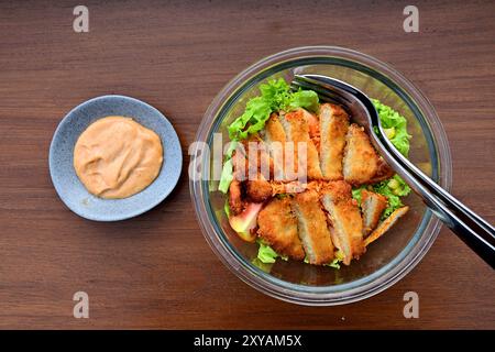 Genießen Sie den Blick auf Salat mit Hühnchen katsu auf der Glasschale, Mayonaise auf der kleinen blauen Platte. Isoliert auf dem Holztisch. Stockfoto