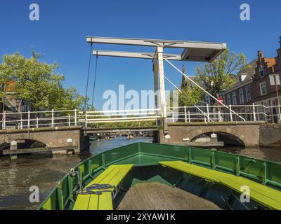 Bootsfahrt unter einer Metallbrücke durch einen malerischen Kanal, gesäumt von historischen Gebäuden und Bäumen, alkmaar, niederlande Stockfoto