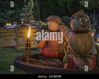Zwei Kürbisskulpturen sitzen auf einem Holzrad, beleuchtet von einer brennenden Fackel im Abendgarten, borken, münsterland, Deutschland, Europa Stockfoto