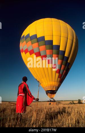 Masai-Krieger beobachten einen Heißluftballon, der auf den Mara Plains im Masai Mara Game Reserve in Kenia landet Stockfoto