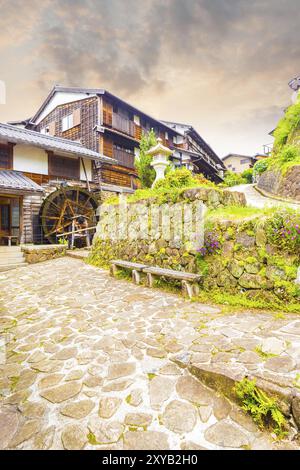 Rustikales Wasserrad und traditionelle Holzhäuser säumen den Steinweg auf diesem restaurierten Abschnitt der historischen Nakasendo-Straße bei Sonnenuntergang im p Stockfoto