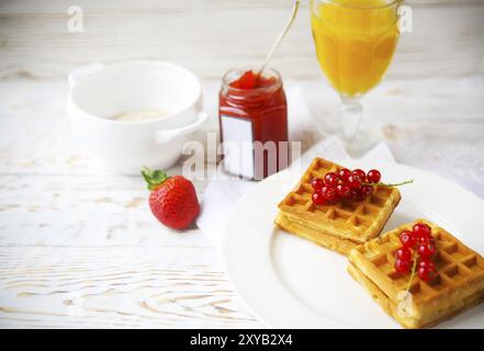 Waffeln mit Johannisbeer-Marmelade und Beeren auf einem weißen Teller, orange Saft und Hafer Flocken Haferflocken auf dem hölzernen Hintergrund Stockfoto