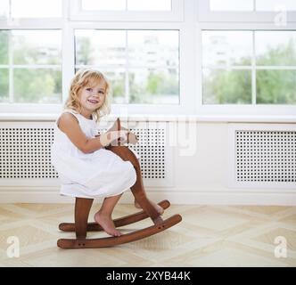 Kleine süße Mädchen im Kinderzimmer mit Holzpferd am Fenster Stockfoto