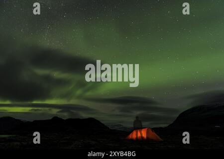 Mann, der vor einem beleuchteten Zelt mit Nordlichtern (Aurora borealis) oben steht, Kebnekaisefjaell, Norrbotten, Lappland, Schweden, September 2012, Stockfoto