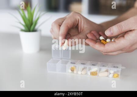 Weibliche ältere Hände, die Pillen sortieren. Nahaufnahme der medizinischen Pillenbox mit Dosen von Tabletten für den täglichen Gebrauch nehmen Sie ein Medikament mit weißen, gelben Medikamenten und Kapseln. Stockfoto