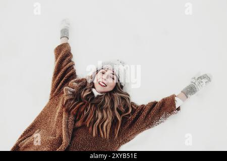 Junge, schöne Frau, die sich im Wickelwald auf dem weißen Schnee niederlegt. Mädchen ist glücklich mit geschlossenen Augen. Weibchen hat Wickler Urlaub und wartet auf C Stockfoto