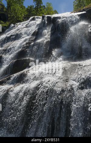 Ein hoher Wasserfall, der über Felsen fließt und in die Tiefe fällt, bei sonnigem Wetter und umgeben von Bäumen, Cascada del Caozo, Garganta de Bonal de los Stockfoto